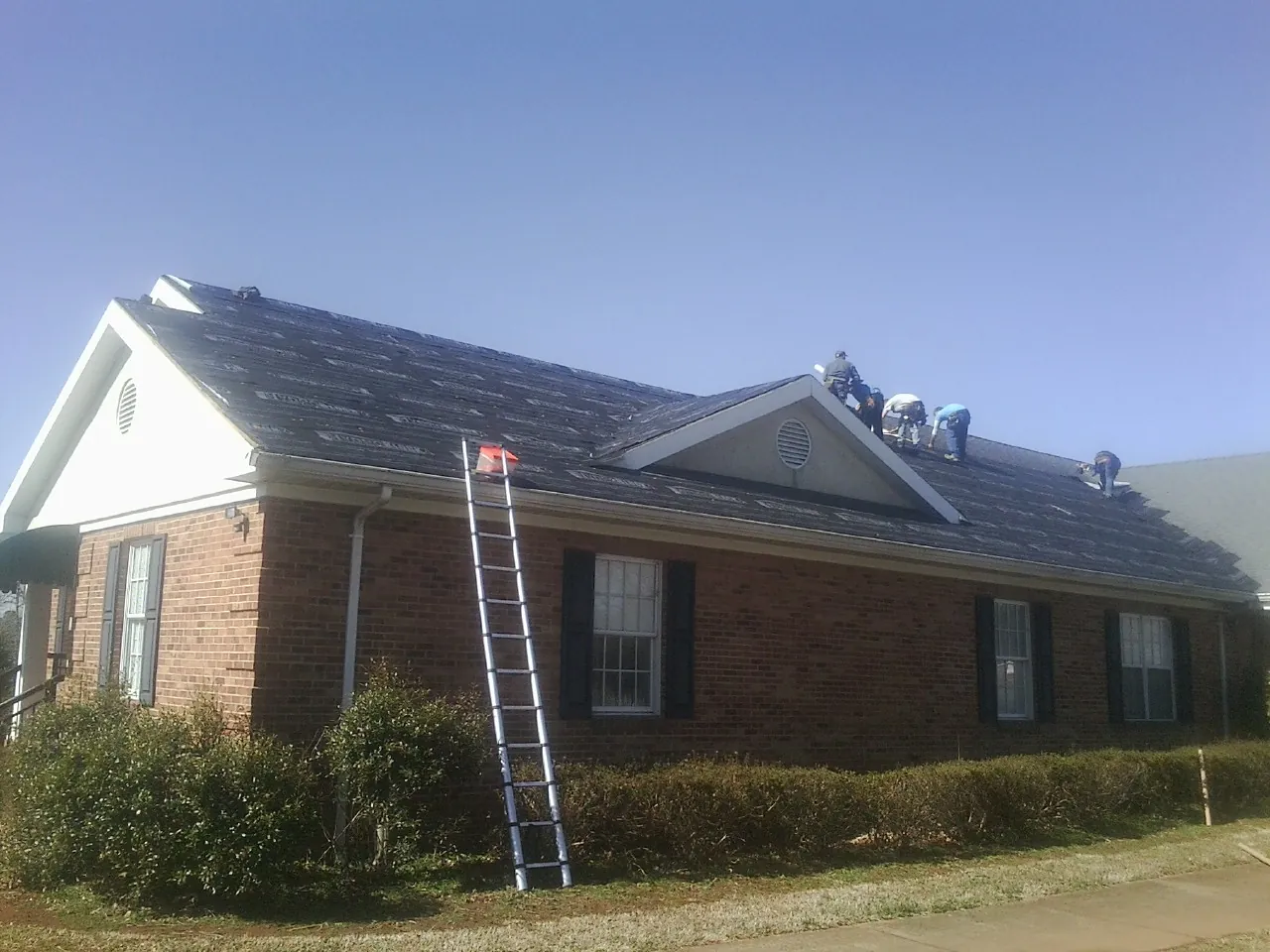 Crew tearing shingles off a brick ranch roof with a ladder set — Emergency Roof Repair work by our crew in Libertyville