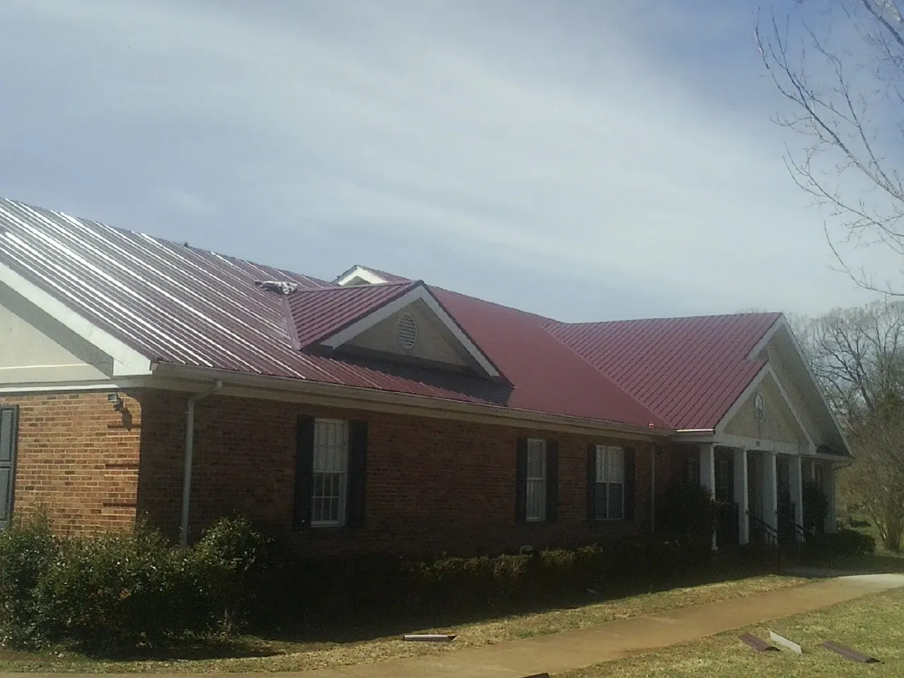 Red metal roof with gabled entries on a long brick building, from a Hail Damage Roof Repair job in Libertyville