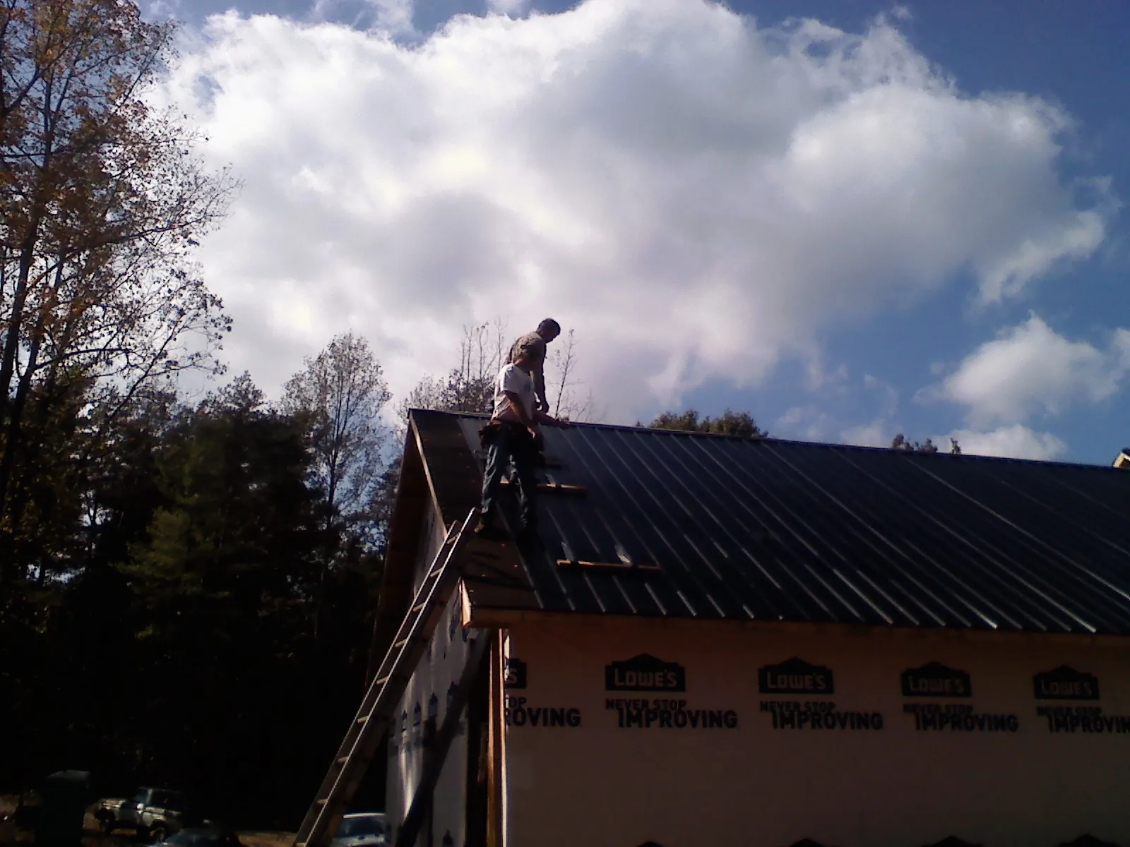 Roofer fastening dark metal panels high against a cloudy sky, from a Roof Inspection job in Libertyville