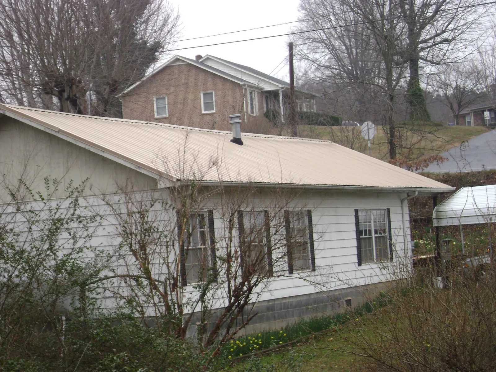 Tan metal roof on a white sided house set into a hillside — Commercial Roofing by Roofing Brothers in Libertyville